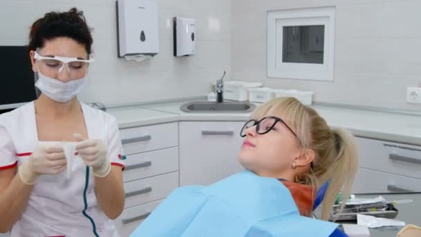 Female dentist preparing mouth expander for young patient with caries — Stock Video