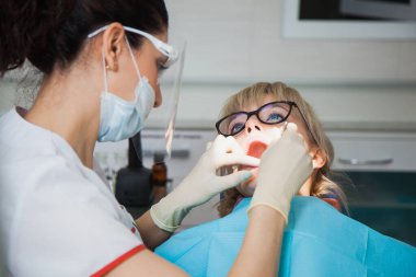 Diş boşluğuyla çalışan koruma maskeli diş hekiminin yakın çekimi..