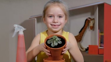 Sevimli küçük kız, sulu bitkiyi daha büyük bir saksıya yerleştirir..