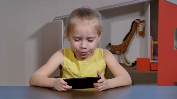 Söt liten flicka spelar spel smartphone inomhus. — Stockvideo