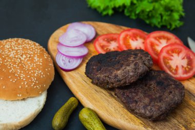 Karanlık masa üzerinde sığır burger malzemeleri seti.