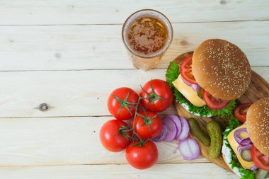 Beyaz ahşap masada bira ve domates dalıyla iki lezzetli hamburger..