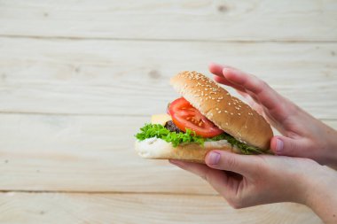 Elleri ahşap masada ev yapımı sığır burger tutuyor..