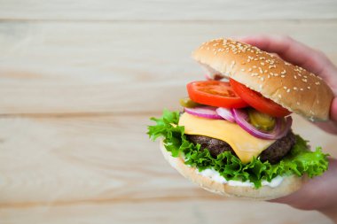 Elleri ahşap masada ev yapımı sığır burger tutuyor..