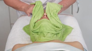 Güzellik uzmanının elleri, sıcak havlu kullanarak güzellik maskesini çıkartır.