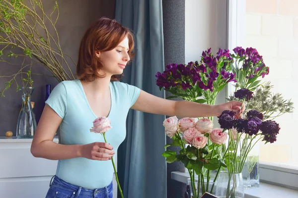 Çiçekçi işte. Mavi bir t-shirt kızıl saçlı kız, gül alışılmadık bir gelinlik buketi oluşturur, alstroemeria, sulu, devedikeni ve scabiosa. Çiçek atölyesi.