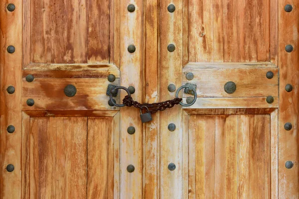 Fragment of old shabby wooden gates with black forged fittings.  Doors are closed. Padlock hanging on a rough rusted chain. The ancient Lycian city of Patara. Turkey.