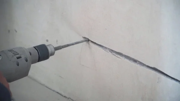 A man drills a concrete wall in an apartment with a drill