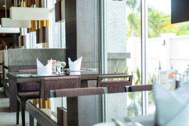 Düzgün düzenlenmiş yemek masaları, katlanmış peçeteler ve büyük pencerelerden gelen doğal ışık, iyi yemek, konukseverlik, yaşam tarzı ve modern mutfak hizmetlerini temsil ediyor..