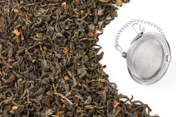 Tea strainer on a chain, with a mixture of dry green large-leaf tea with soursop, isolated on a white background. A tea filter is a close-up of a kitchen accessory.