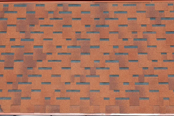 The texture of the roof with bituminous coating. Rough bituminous mosaic of red and brown flowers. Waterproof roofing.