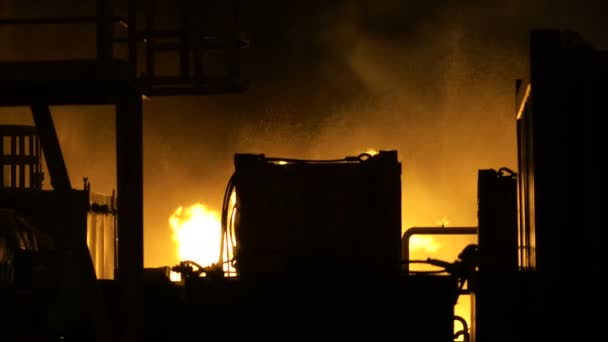 Пламя горит за металлическими конструкциями промышленного здания ночью — стоковое видео