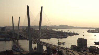 Üzerinde bir çok arabanın seyahat ettiği kablo destekli otomobil köprüsü üzerinde bir vinç gemisinin yüzdüğü boğazın üzerinde duruyor.