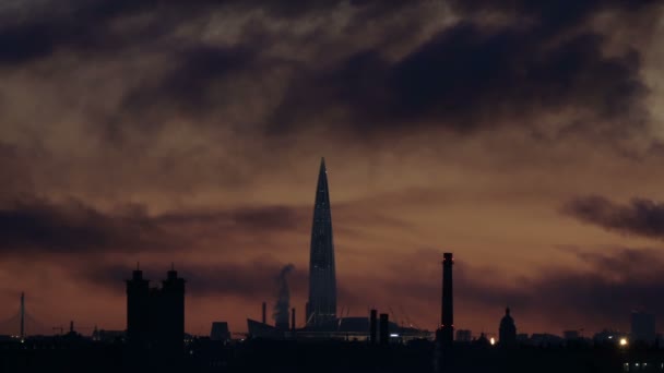 La fumée noire vole au vent au-dessus d'une ville industrielle avec un grand gratte-ciel, debout en silhouette au coucher du soleil, flammes visibles — Video