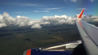Alçalmakta olan uçağın kanat ve türbininin görüntüsü, şimdiden Cumulus bulutları seviyesinde uçuyorum. Yeşil ormanlarda bulut gölgeleri görünür.