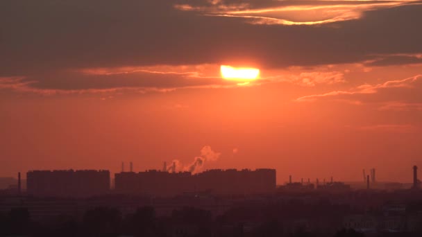 El sol se pone detrás de una nube y se pone sobre el horizonte sobre el telón de fondo de una zona industrial. Humo de las pipas, niebla y niebla del calor. — Vídeos de Stock