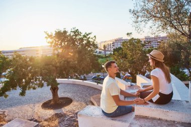Oturma ve elele zemin üzerine panoramik şehir manzaralı günbatımında genç mutlu çift.