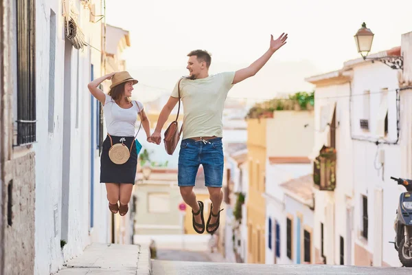 Happy and funny young couple of travellers jumping when walking in old Spanish town.