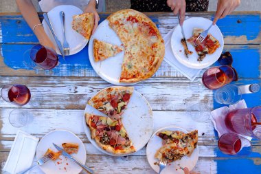 Üstten görünüm grup arkadaşıyla açık havada restoranda pizza ile masada yemek yiyorlar. Yemek ve eğlence kavramı.