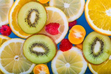 Taze ahududu, mandarin, kivi, portakal, limon ve portakal dilimleri mavi suda yüzer. Sulu ve renkli meyve deseni.