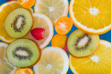 Taze ahududu, mandalina, kivi, portakal, limon ve portakal dilimleri mavi suda yüzer. Sulu ve renkli meyve deseni.