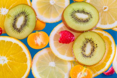 Taze ahududu, mandalina, kivi, portakal, limon ve portakal dilimleri mavi suda yüzer. Sulu ve renkli meyve deseni.