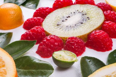 Çiçekler beyaz izole sulu narenciye yapılan Close-up. Portakal, limon, kivi, mandarin ve ahududu. Renkli ve taze kompozisyon. Meyve deseni.