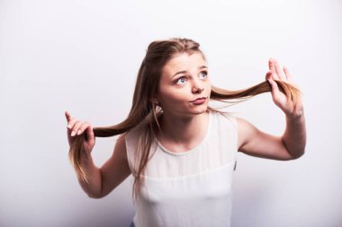 Beyaz t-shirt yapması ve saç ışık gri arka plan üzerinde tutarak iri gözlü genç neşeli ve komik kadın.