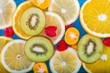 Taze ahududu, mandalina, kivi, portakal, limon ve portakal dilimleri mavi suda yüzer. Sulu ve renkli meyveler.