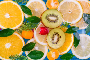 Taze ahududu, mandalina, kivi, portakal, limon ve portakal dilimleri mavi suda yüzer. Sulu ve renkli meyveler.