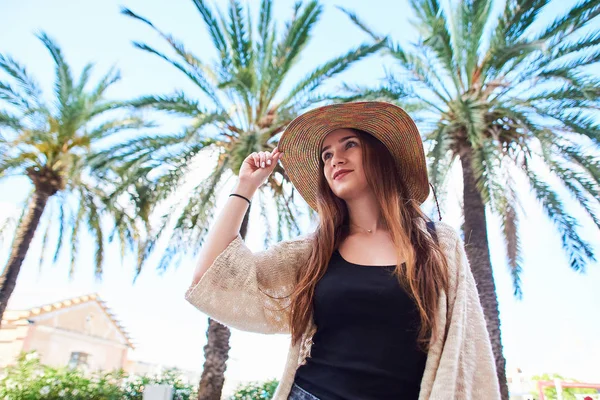 年轻漂亮的女孩在草帽里微笑着 在夏日阳光明媚的日子里 映衬着棕榈树和蓝天 旅行和度假概念 — 图库照片