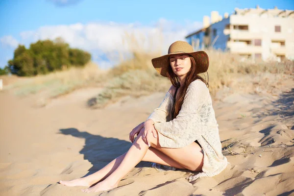 年轻迷人的黑发妇女穿着时髦的草帽坐在阳光下 在沙滩上放松 — 图库照片