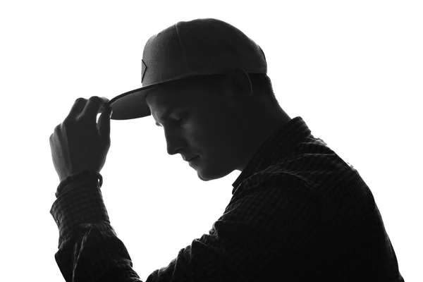 Side face of a young thoughtful man holding his hand on a cap. Silhouette. Black and white.