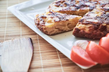 Geleneksel İspanyol omleti Close-up tortilla de patatas domates ile beyaz tabakta aradı. Yumurta, patates ve soğan yapılmış omlet.