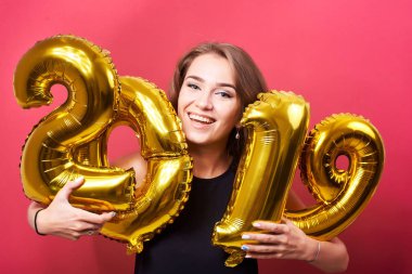 Yeni yıl kutlama ve kırmızı zemin üzerine altın 2019 balonlarla eğleniyor genç çekici kadın.