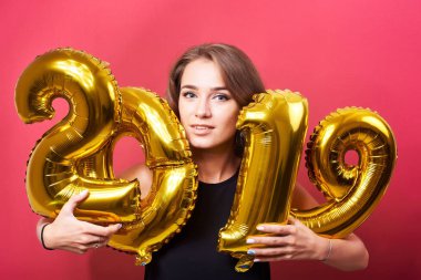 Yeni yıl kutlama ve kırmızı zemin üzerine altın 2019 balonlarla eğleniyor genç mutlu kadın portresi.