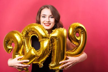 Yeni yıl 2019 kutluyor ve ellerinde kırmızı zemin üzerine altın balonlar tutan parlak kalıcı makyaj ile genç gülümseyen kadın.