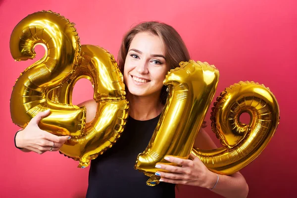 Yeni yıl kutlama ve kırmızı zemin üzerine altın 2019 balonlarla eğleniyor genç çekici kadın.