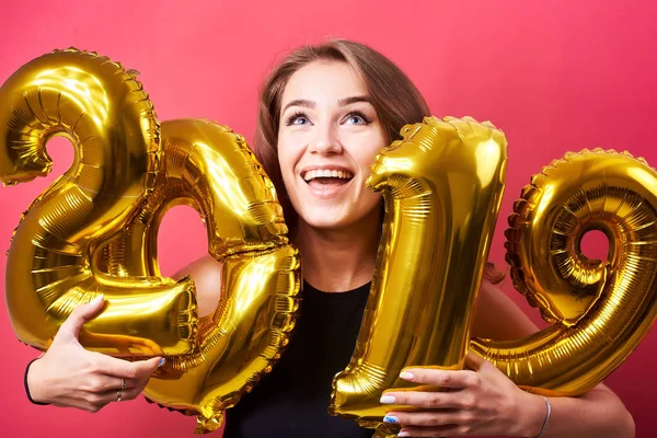 年轻的有吸引力的妇女庆祝新年和有乐趣与金黄2019年气球在红色背景 — 图库照片