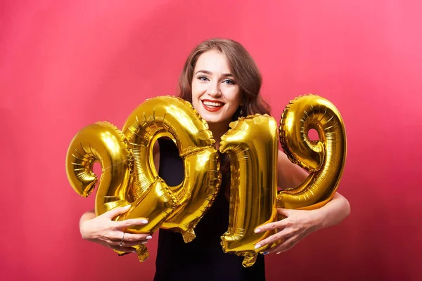 年轻的微笑的女人与明亮的化妆庆祝2019年新年 并拿着金色气球手在红色的背景 — 图库照片