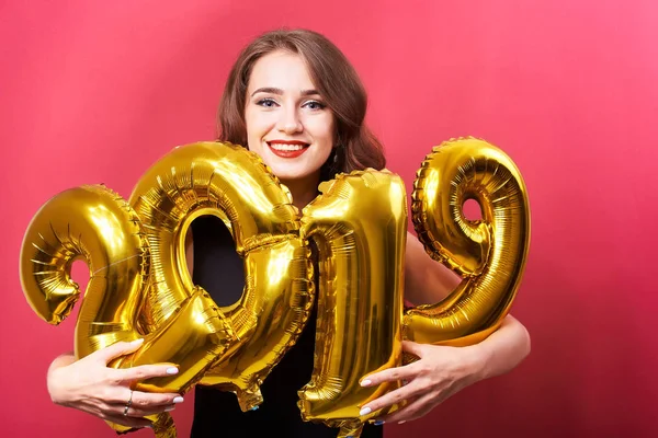 Yeni yıl 2019 kutluyor ve ellerinde kırmızı zemin üzerine altın balonlar tutan parlak kalıcı makyaj ile genç gülümseyen kadın.