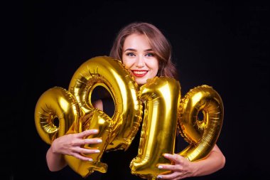 Genç gülümseyen kız eğleniyor ve altın balonlar siyah arka plan üzerine elinde tutan parlak makyajlı. Yeni yıl 2019 kutlama.