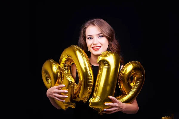 一个年轻的微笑的女人的肖像与明亮的化妆有乐趣 并拿着金色气球手在黑色的背景 2019年新年庆祝活动 — 图库照片