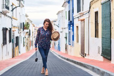 Hasır şapka ve eski fotoğraf makinesi onun elinde tutan ve İspanyol şehrin Denia küçük renkli binalar ile eski kesiminde yürüme genç mutlu uzun saçlı kadın.