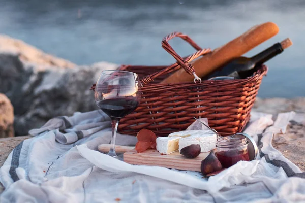 Picnic basket with red wine, bread, jam, cheese and jamon. Romantic picnic on the beach with sea on background.