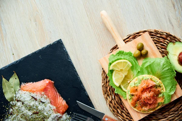 Ahşap tahta üzerinde bir lezzetli taze tuzlanmış somon fileto crispbread ve avokado ile en iyi görünümü. Aromatik otlar, baharatlar ve sebzeler - sağlıklı gıda, diyet ve pişirme kavramı.