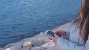Denizin üzerinde bir arka plan ile bir cep telefonuyla mesaj yazarken eller Close-up.