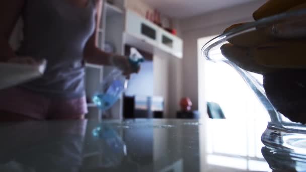 Домохозяйка распыляет моющее средство и вытирает стеклянный стол — стоковое видео