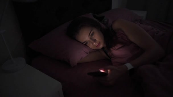 Młoda kobieta z telefonu komórkowego w nocy w łóżku — Wideo stockowe