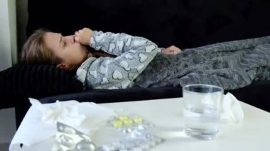 Dinamik video evde koltukta oturan, öksürük ve burun üfleme genç hasta bir kadın. İlaçlar tablo.